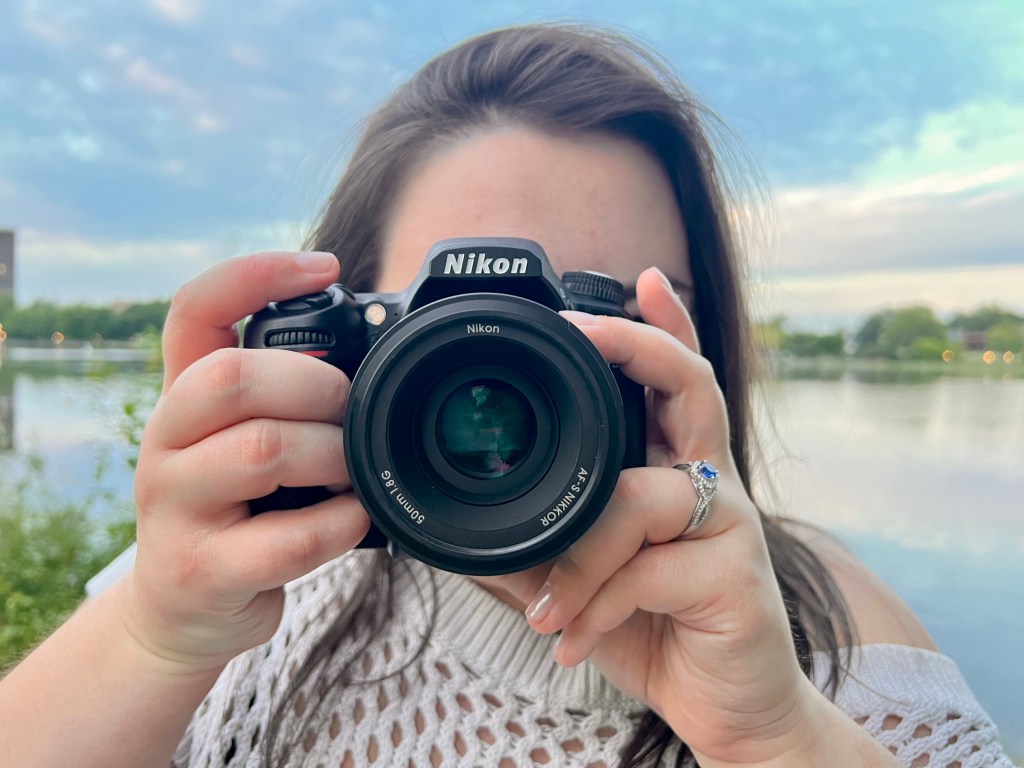 Abbey holding her Nikon camera with a lake behind her